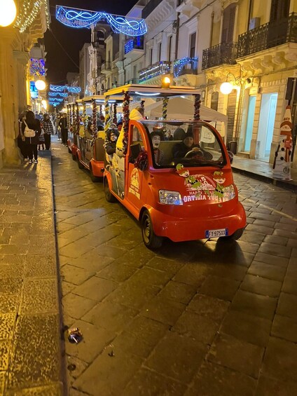 A red car decorated with festive ornaments and a Santa hat, parked on a cobblestone street at night. 2