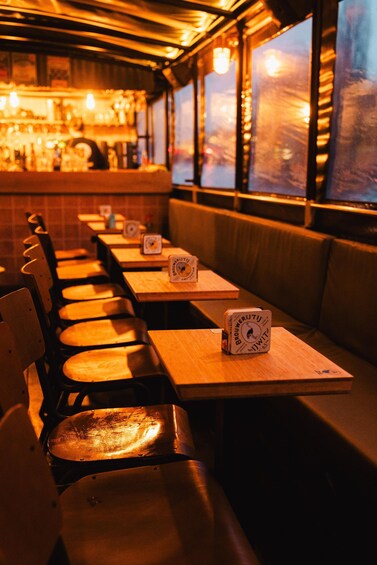 A dimly lit restaurant with wooden tables and benches, and a bar in the background. 2
