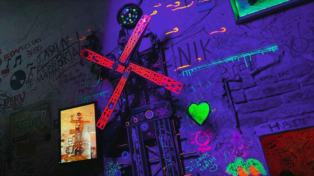 A graffiti-covered wall with a neon cross, a heart, and various writings. 4
