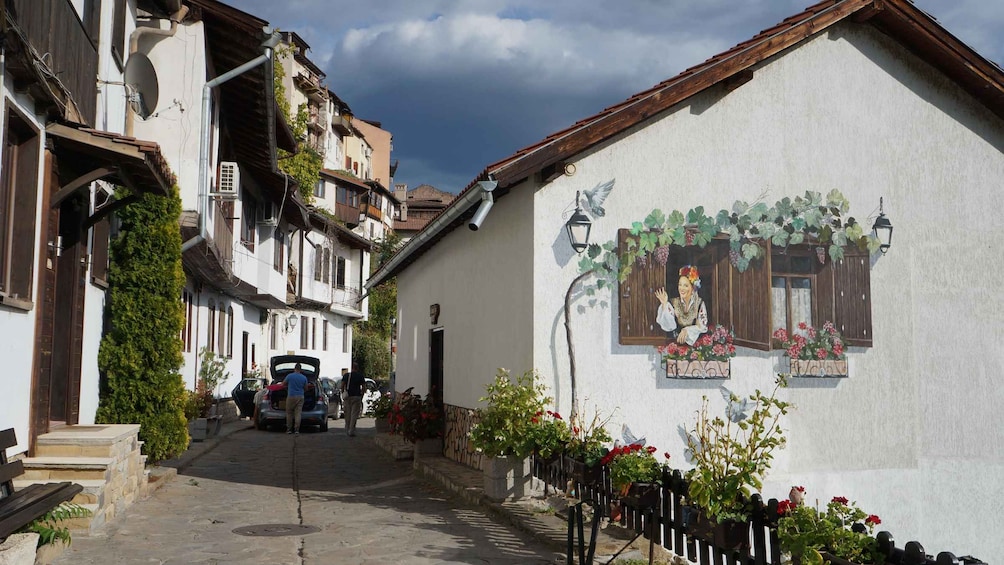 A narrow street with traditional buildings, a mural on a wall, and a man opening a car door. 4