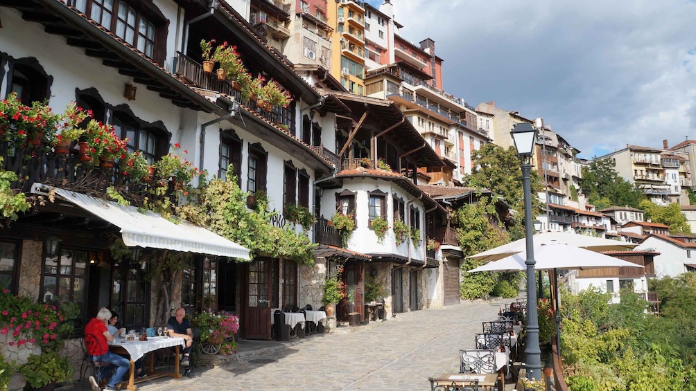 A cobblestone street lined with traditional buildings, outdoor seating, and potted plants. 1