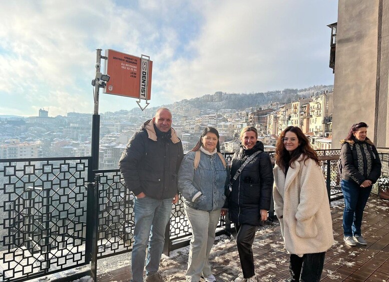 A group of people standing on a balcony with a cityscape in the background. 4