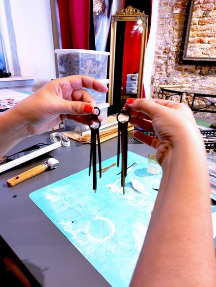 Hands holding a pair of scissors and a ruler on a desk with a blue mat, a bottle, and a mirror in the background. 3