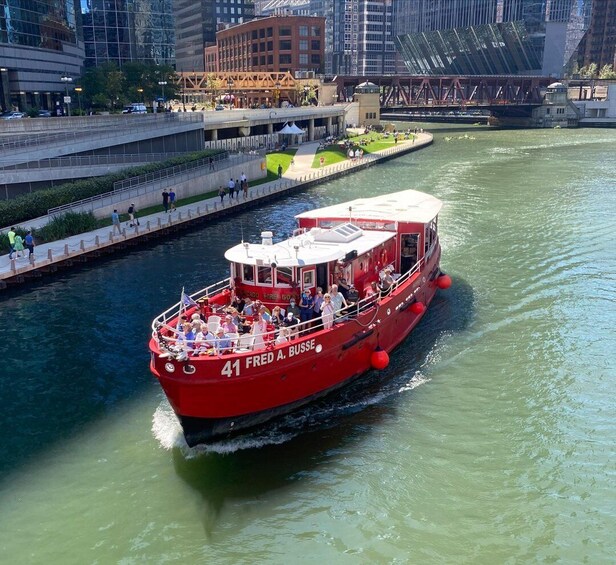 A red boat named 'Fred A. Busse' on a river, surrounded by city buildings and a pedestrian walkway. 3