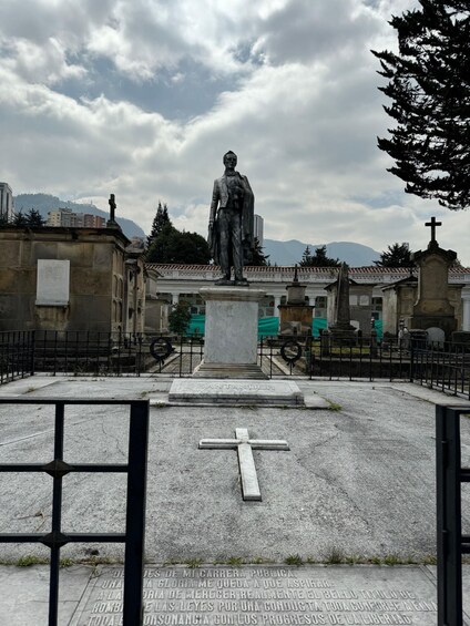 A statue of a man in a suit with a cross on top, surrounded by a fence and a cross on the ground. 2