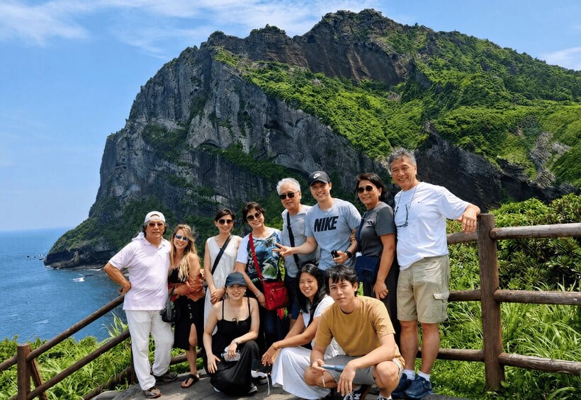 A group of people posing on a wooden staircase with a mountainous landscape and ocean in the background. 3