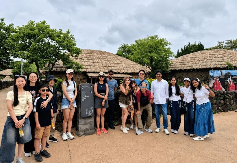 A group of people posing in front of traditional huts with thatched roofs. 5