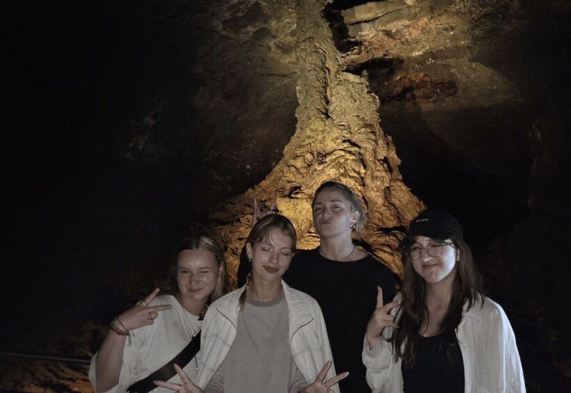 A group of people standing in front of a cave with a rough, textured rock formation. 2
