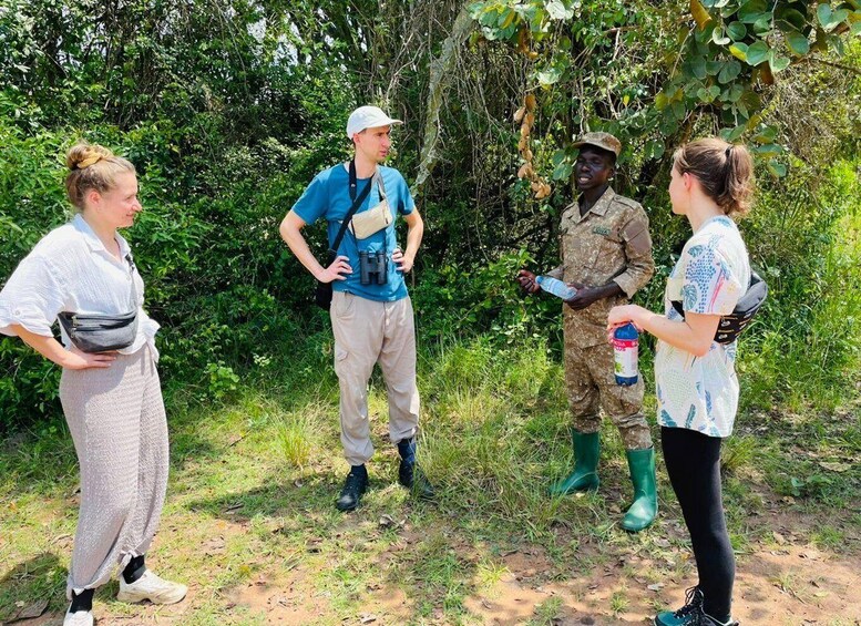 Four people standing outdoors, one in military uniform and others in casual clothing, surrounded by greenery. 4