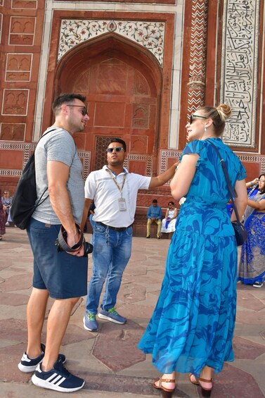 Three people standing in front of a large, ornate building with intricate designs and Arabic script. 3