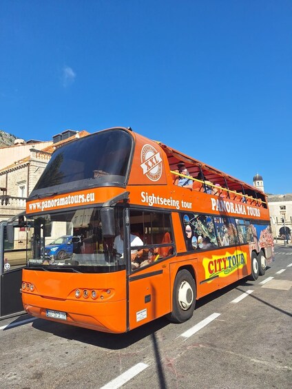 An orange sightseeing tour bus with "Panorama Tours" and "City Tour" branding, parked on a street. 1
