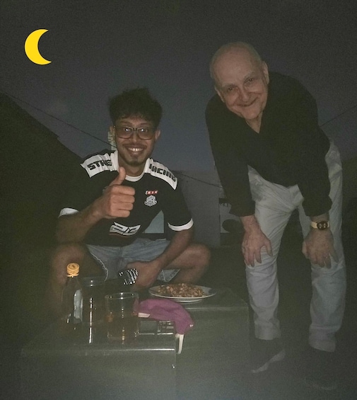 Two people at a table with food and drinks, a crescent moon in the background. 5