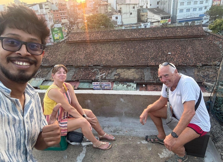 Three people sitting on a rooftop with a traditional tiled roof and a cityscape in the background. 2