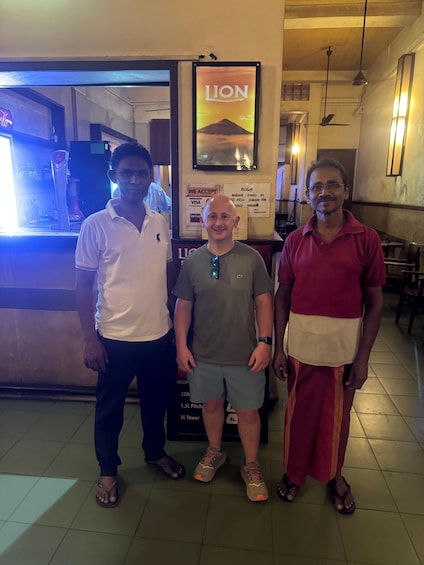 Three people standing in a restaurant with a sign reading 'LION' above them. 4