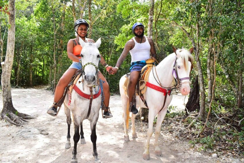 Two people riding horses on a dirt path through a forest. 5
