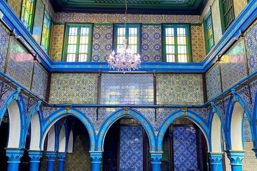 Un interior ricamente decorado con azulejos azules y dorados, arcos y una araña. 2