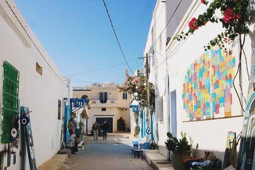 Una calle estrecha con edificios blancos, un mural colorido y un portón azul. 3