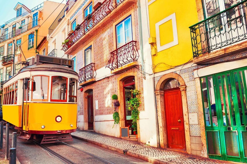 A yellow tram on a street with colorful buildings, including a red door and green shutters. 2