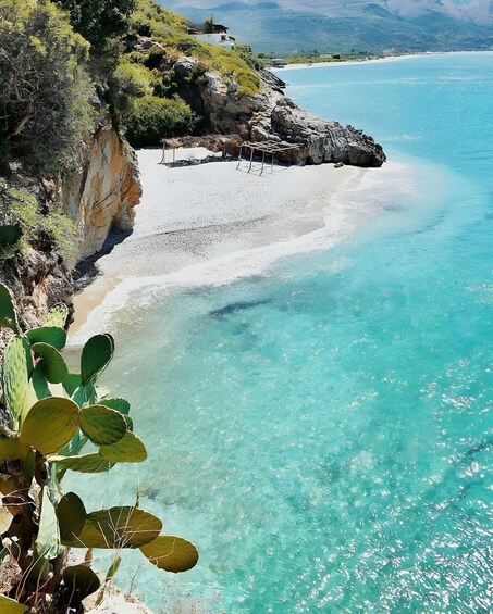 A coastal landscape with clear turquoise waters, a sandy beach, and rocky cliffs. 3