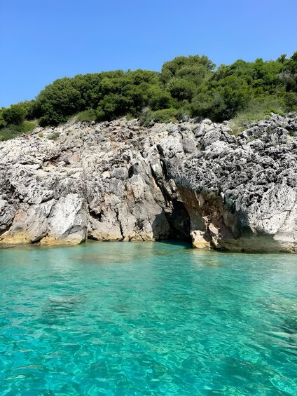 A rocky coastline with clear turquoise water and dense green foliage in the background. 2
