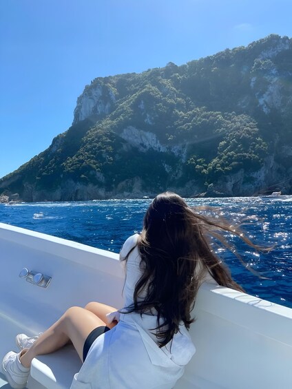 A person on a boat with a mountainous coastline in the background. 1