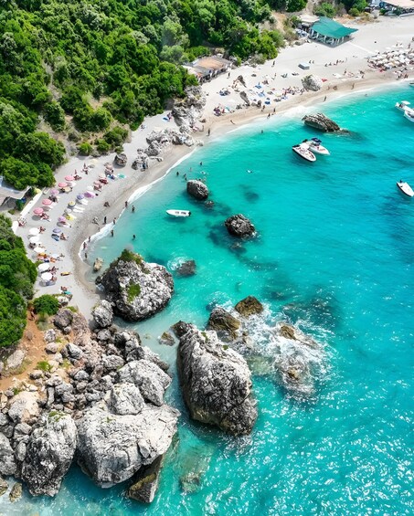 A coastal beach with clear turquoise waters, rocky outcrops, and numerous umbrellas. 5