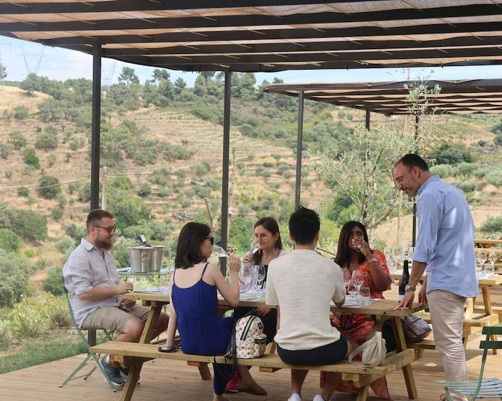 A group of people dining outdoors on a wooden deck with a scenic hillside in the background. 5