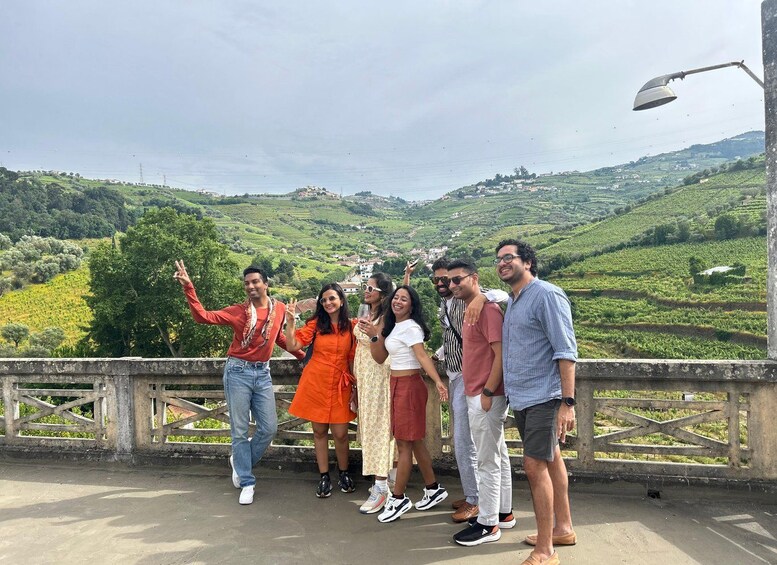 A group of people on a bridge with a scenic view of green hills and vineyards. 1