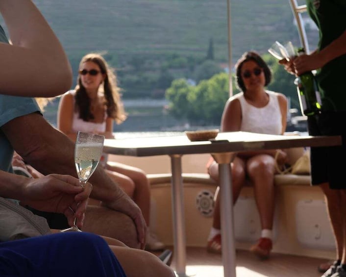 A group of people on a boat, some holding drinks, with a view of a body of water and greenery in the background. 3
