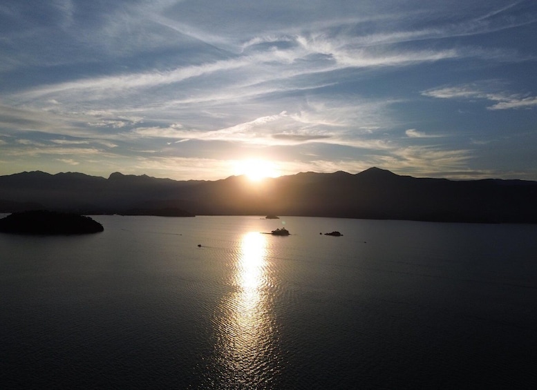 A calm lake with the sun setting behind mountains, creating a silhouette effect. 5