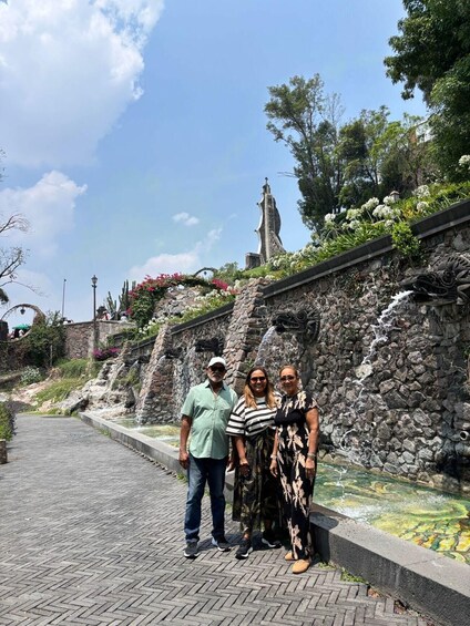 A stone wall with a waterfall, a statue, and a paved pathway. 2