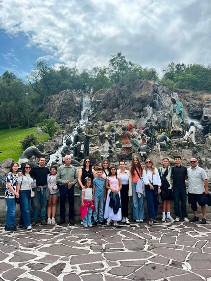 A group of people standing in front of a waterfall and statues in a natural setting. 1