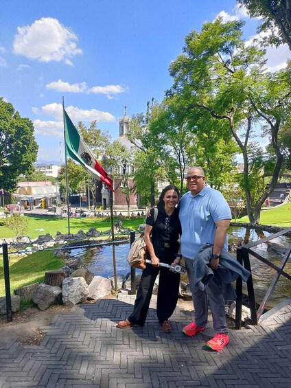A couple standing by a pond with a church and flag in the background. 3