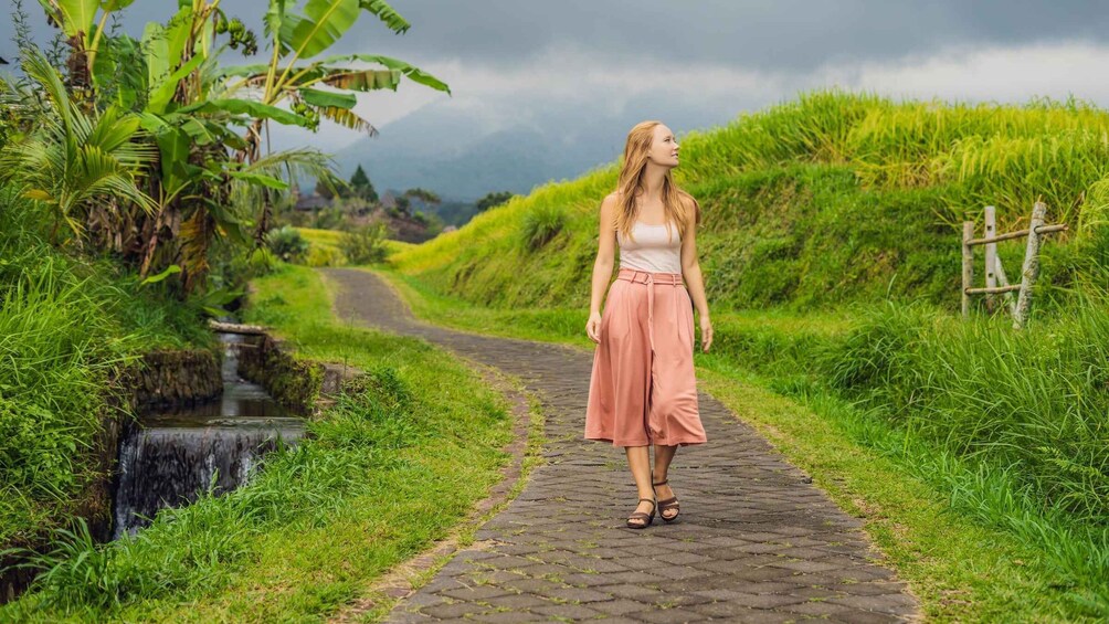 A woman walking on a cobblestone path surrounded by lush greenery and a small stream. 4