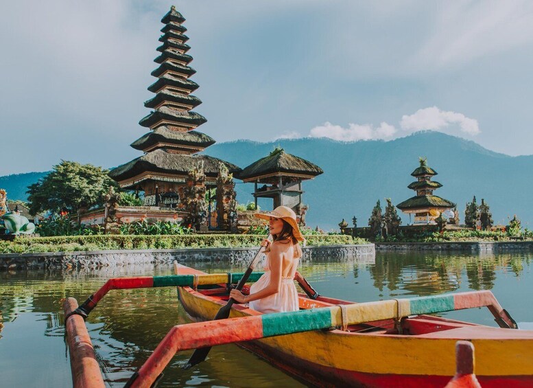 A woman in a boat on a calm lake with traditional Balinese temples in the background. 1