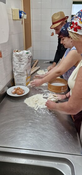 Two people kneading dough on a stainless steel countertop in a kitchen. 1
