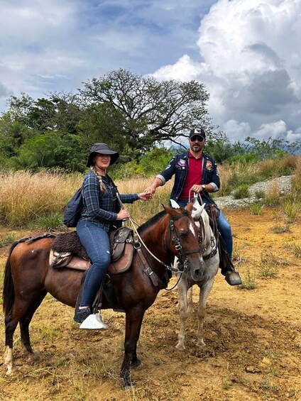 Two people riding horses on a dirt path with trees and a cloudy sky in the background. 2
