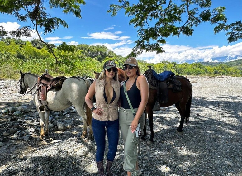 Two people standing next to horses on a gravel path with trees and a clear sky in the background. 5