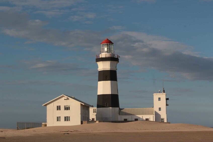 A lighthouse with a red top, a white building with a flat roof, and a smaller white structure with a red roof. 1
