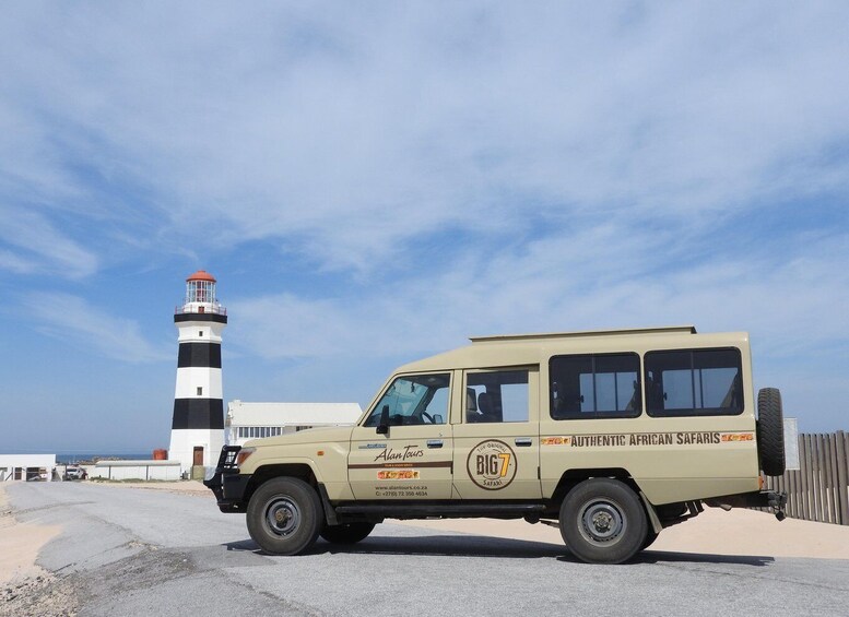 A beige safari vehicle parked near a lighthouse. 4