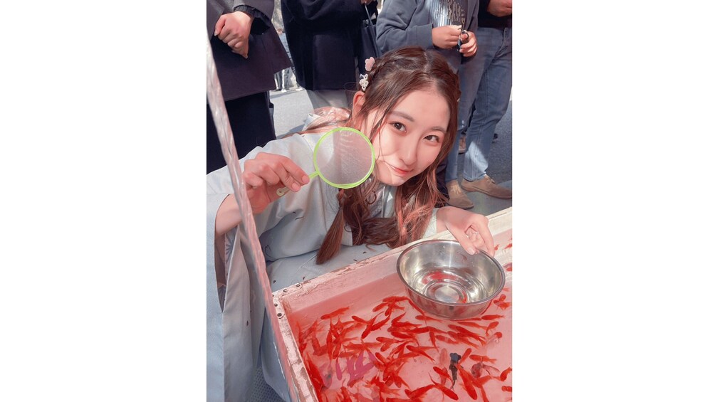 A person holding a net over a bowl of red fish. 4