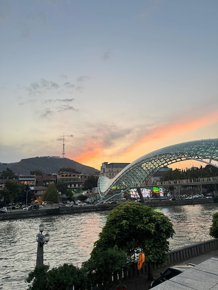 A modern bridge with a glass canopy, a river, and a sunset in the background. 1