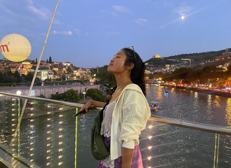 A person standing on a bridge overlooking a river with city lights in the background. 3