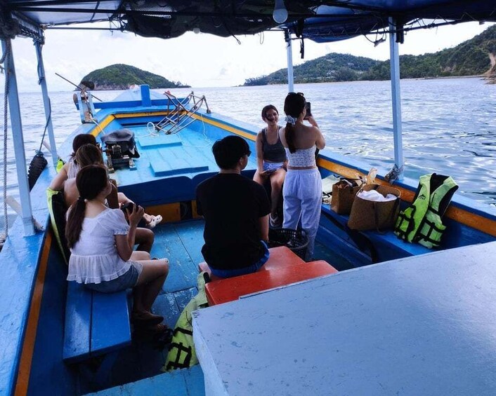 A group of people on a boat with a blue and yellow hull, some wearing life jackets, and a person taking a photo. 4