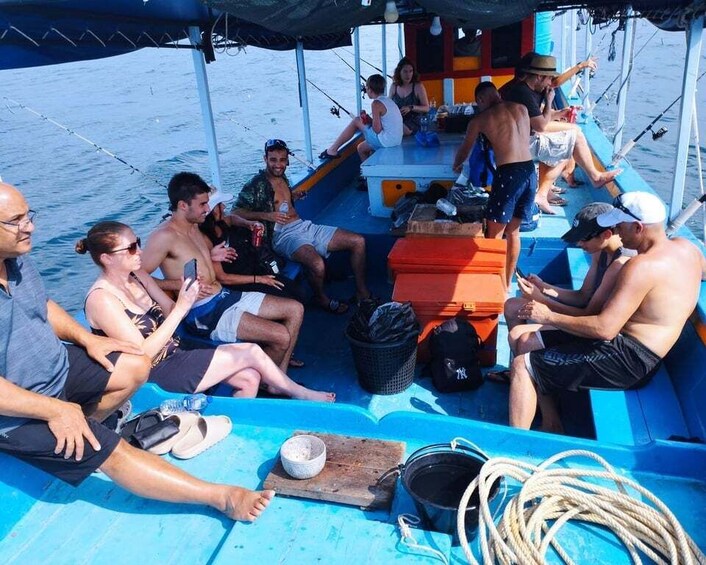 A group of people on a boat with a blue deck, some sitting and others standing, engaged in conversation. 2