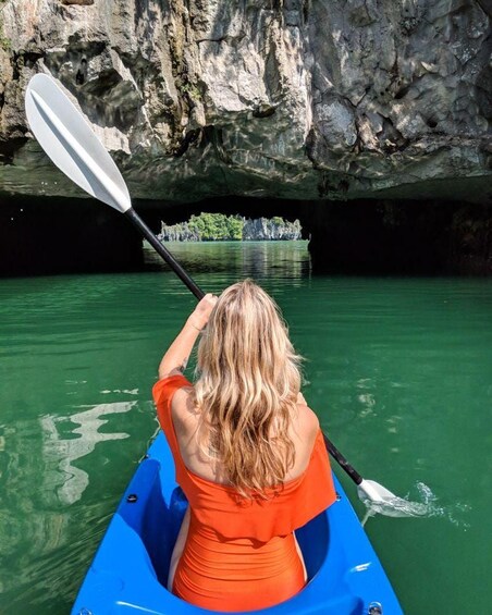 A person kayaking in a blue kayak with an orange shirt, paddling through a greenish water body with rocky cliffs in the background. 3