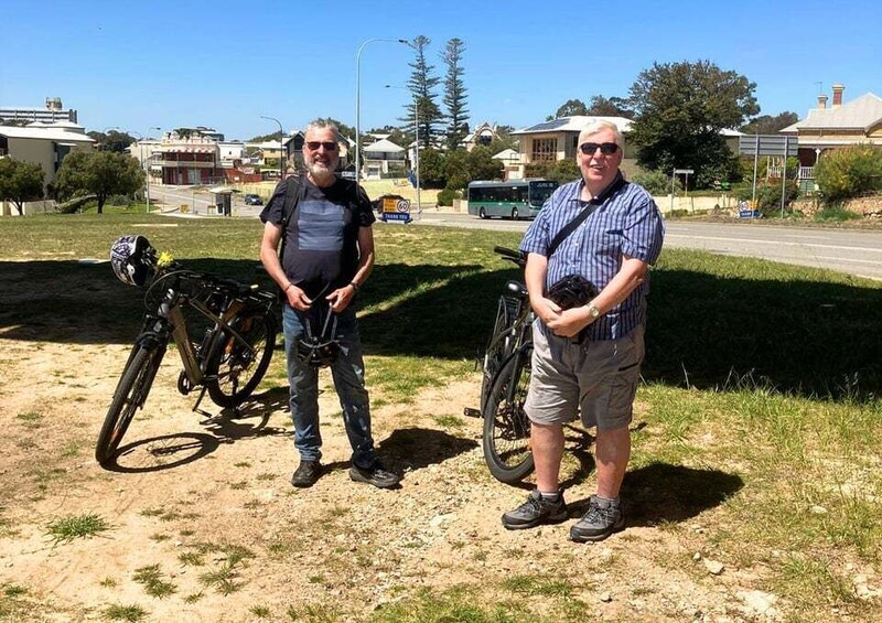 Two men standing on a dirt path with bicycles. 2