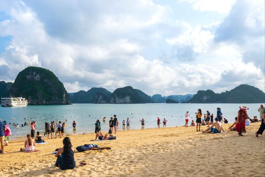 A crowded beach with people sunbathing and swimming, surrounded by lush green hills and a boat in the water. 4