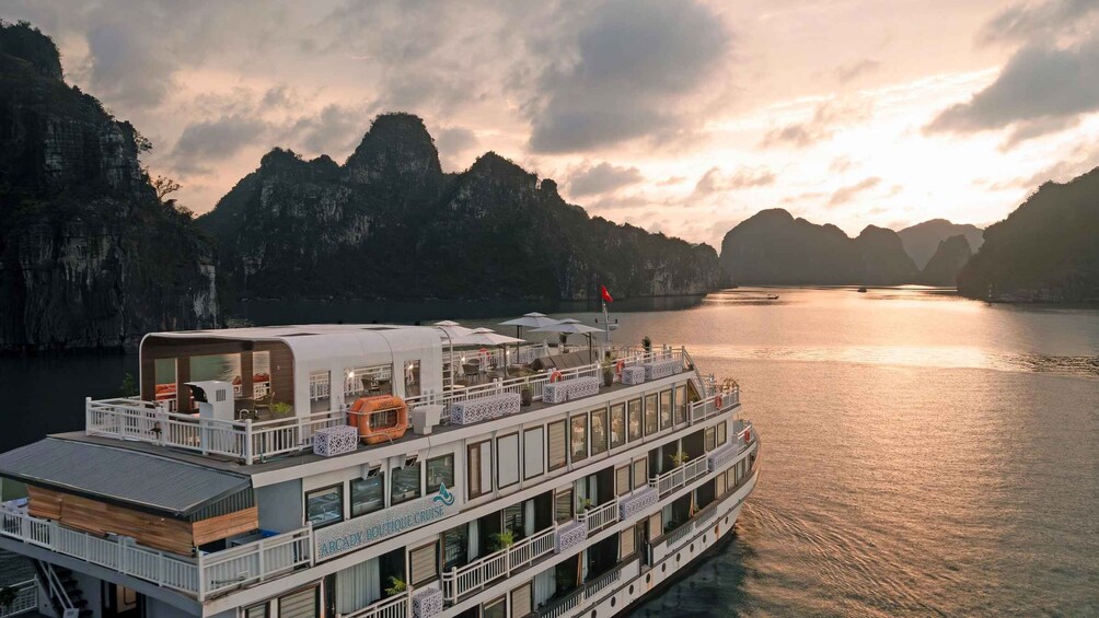 A cruise ship with multiple decks and a restaurant area, sailing in a bay with mountainous terrain in the background. 2