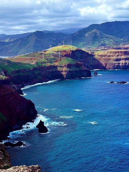 A coastal landscape with wind turbines, rocky cliffs, and a clear blue sea. 4